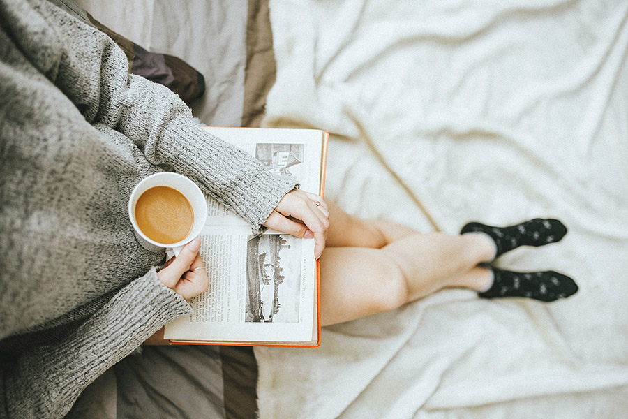 someone sitting down reading a book with coffee in one hand