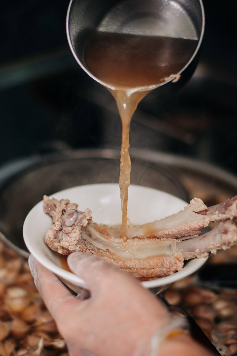 Someone pouring soup into a bowl of pork ribs to make Bak Kut Teh