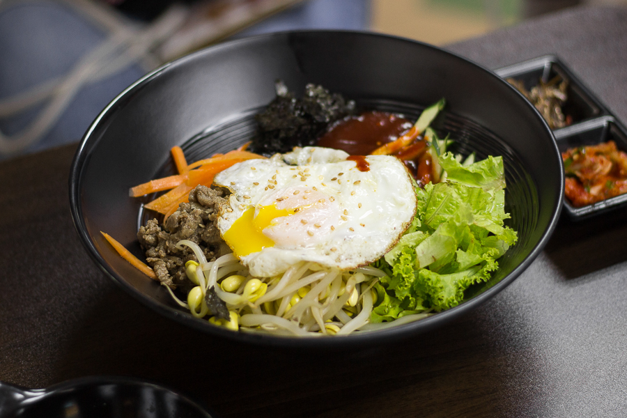 A bowl of bibimbap with ingredients like beansprouts, lettuce, carrots, seaweed and a fried egg