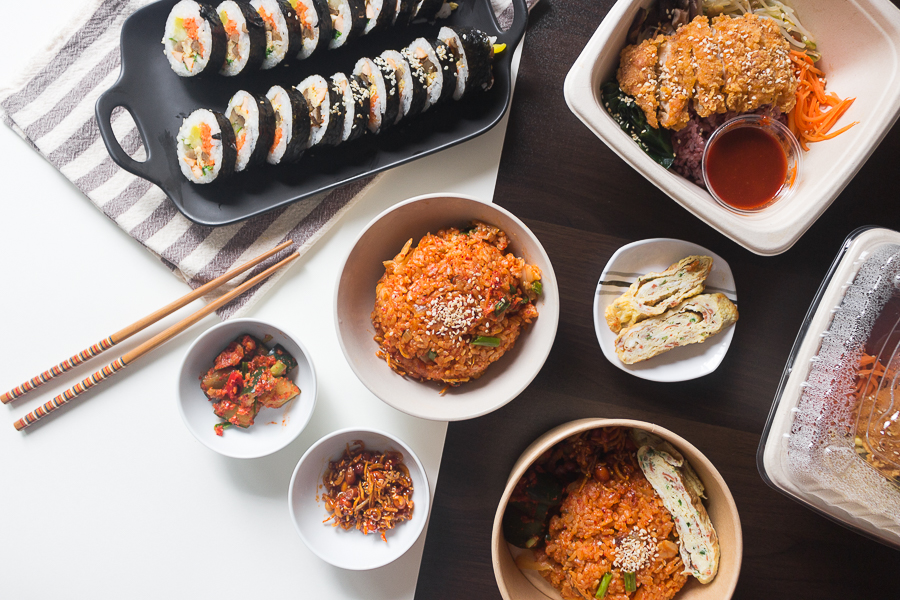 A flatlay of Korean dishes like Kimchi Fried Rice, Gimbap and Chicken Katsu Bibimbap along with a couple of side dishes