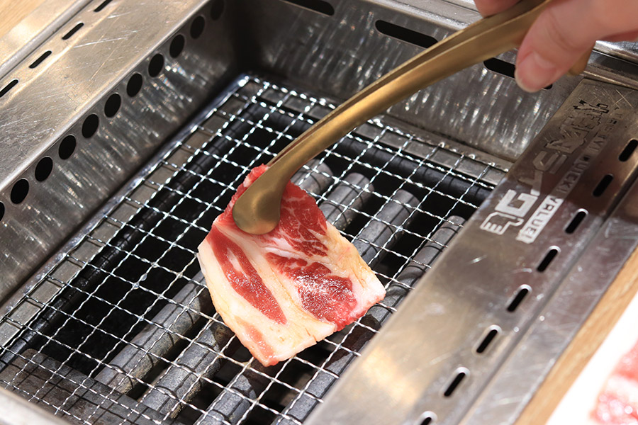 A golden tong placing a piece of meat over a fire at Yakiniku Like in PLQ Mall Singapore