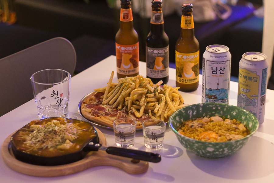 A table filled with menu items from 82 Place such as Ramyeon, half and half pizza and korean craft beers