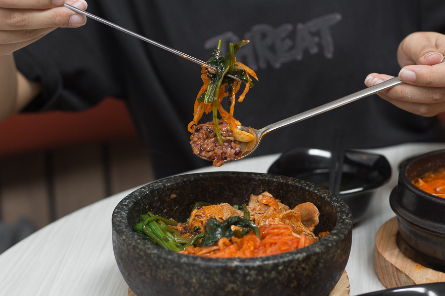 A bowl of brown rice bibimbap in Singapore with spinach, radish kimchi and stir fried pork