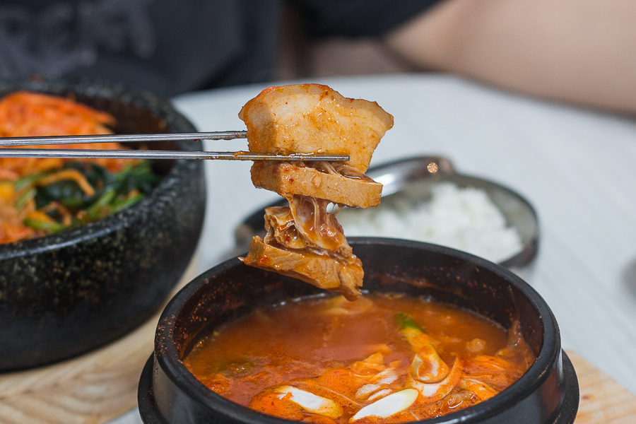 Chopsticks holding a piece of pork belly from the Kimchi Pork Belly Stew over at KimchiXpress Suntec