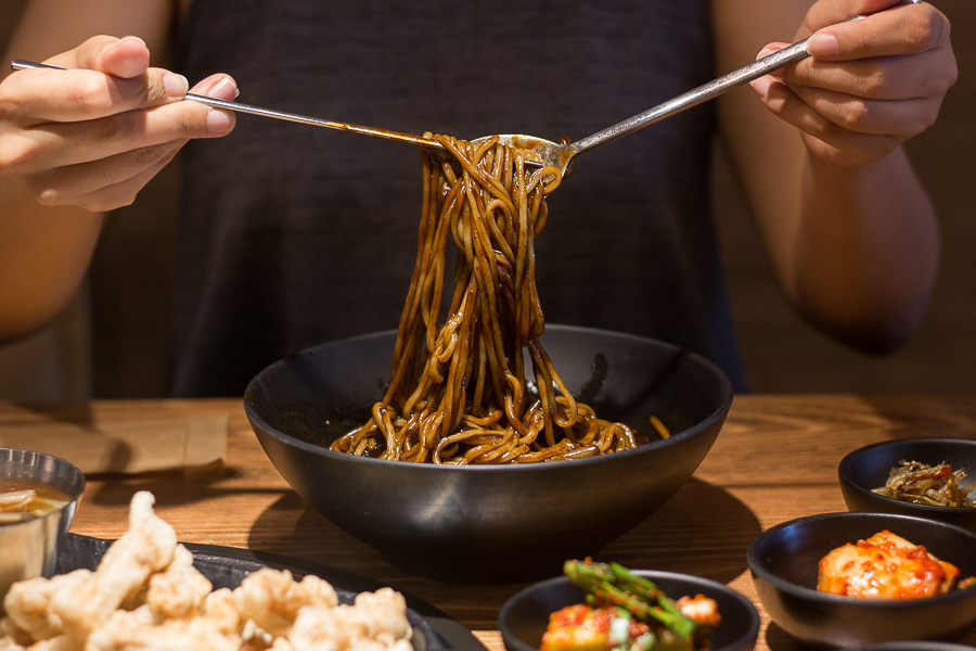 Someone using chopsticks and spoon to lift up the Jjajangmyeon at Taste of Korea JJIN Telok Ayer