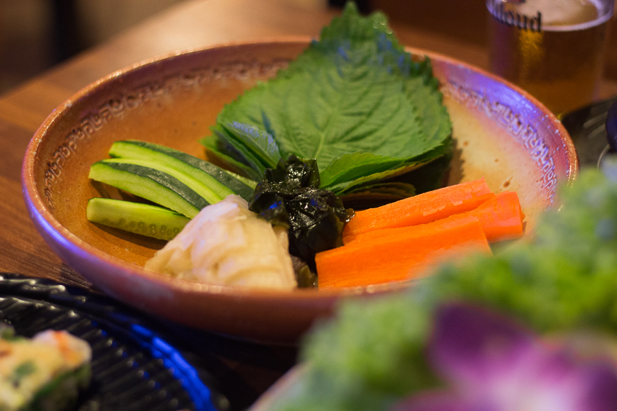 A plate of vegetables containing perilla leaves, cucumber and carrot strips, white kimchi and seaweed