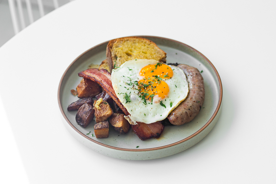 A breakfast platter from Coexist, with sausage, bacon, sunny side up, potatoes and mushrooms