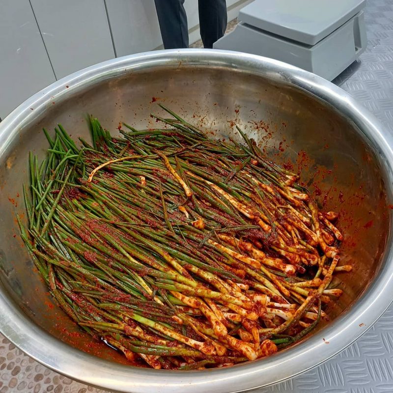 A metal basket filled with green onion kimchi