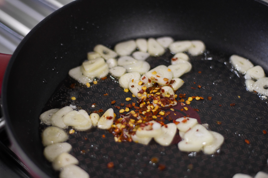 Putting sliced garlic and chilli flakes in a pan with olive oil