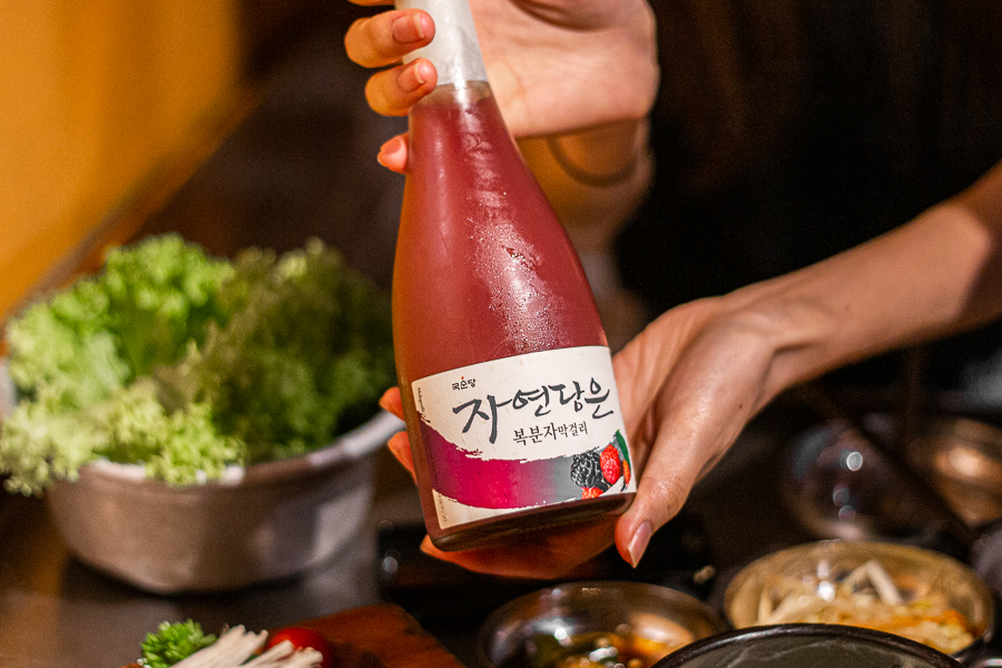 Someone holding a bottle of Bokbunja Makgeolli