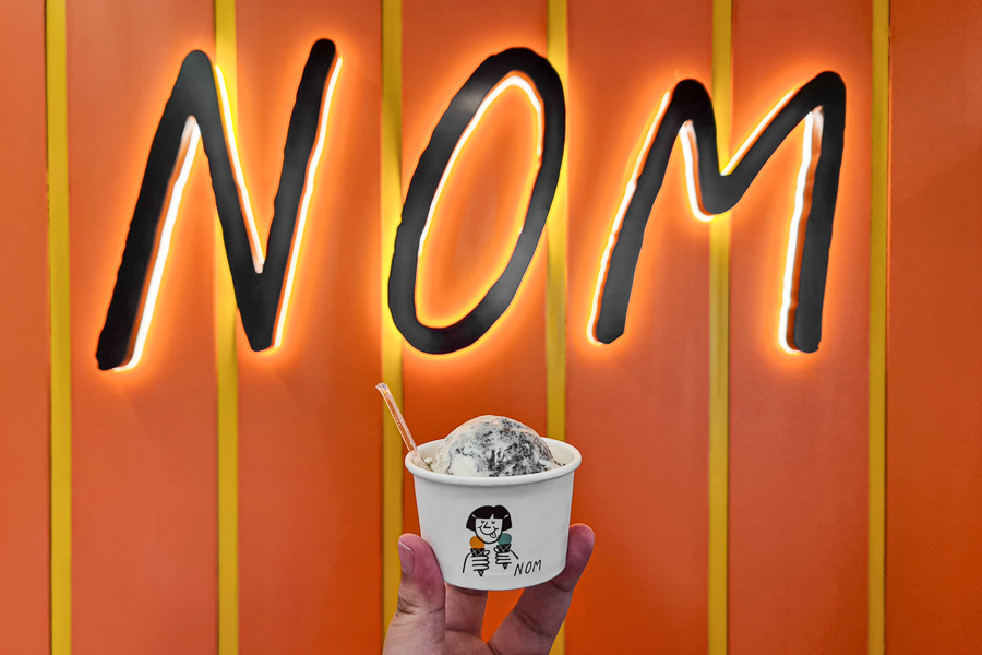 Scoop of NOM Gelato with NOM signage at the back