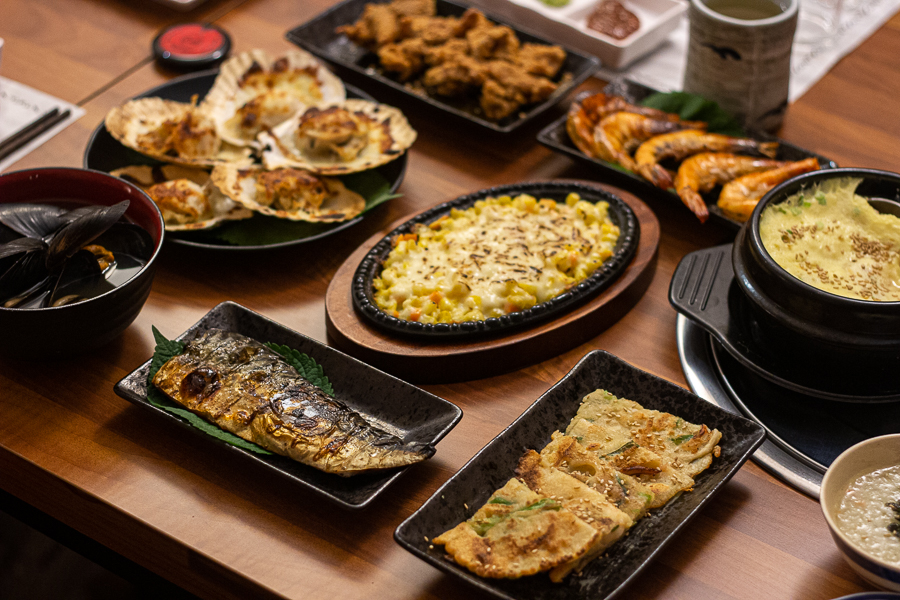 Table filled with corn cheese, korean pancakes, grilled prawns and scallops, grilled fish and a plate of deep-fried chicken skin