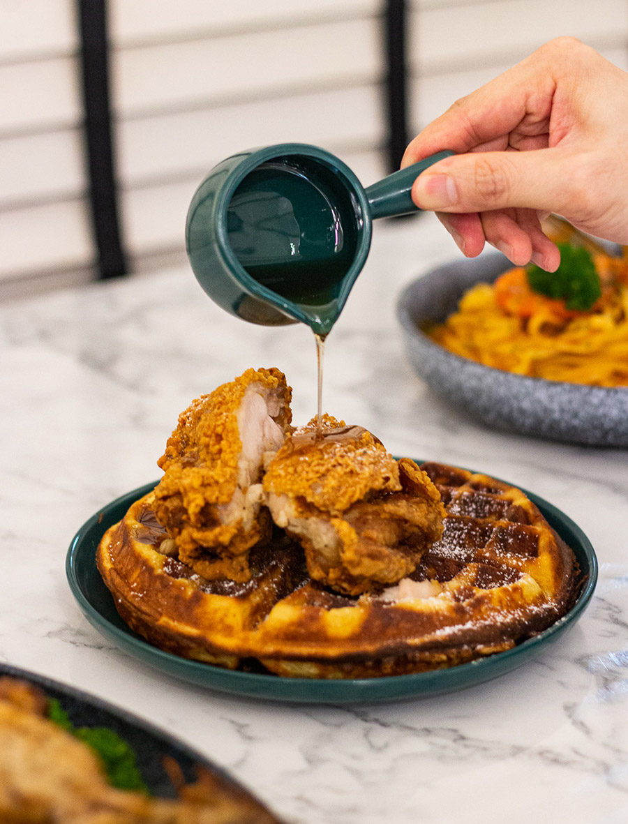 Pouring maple syrup onto fried chicken and waffles