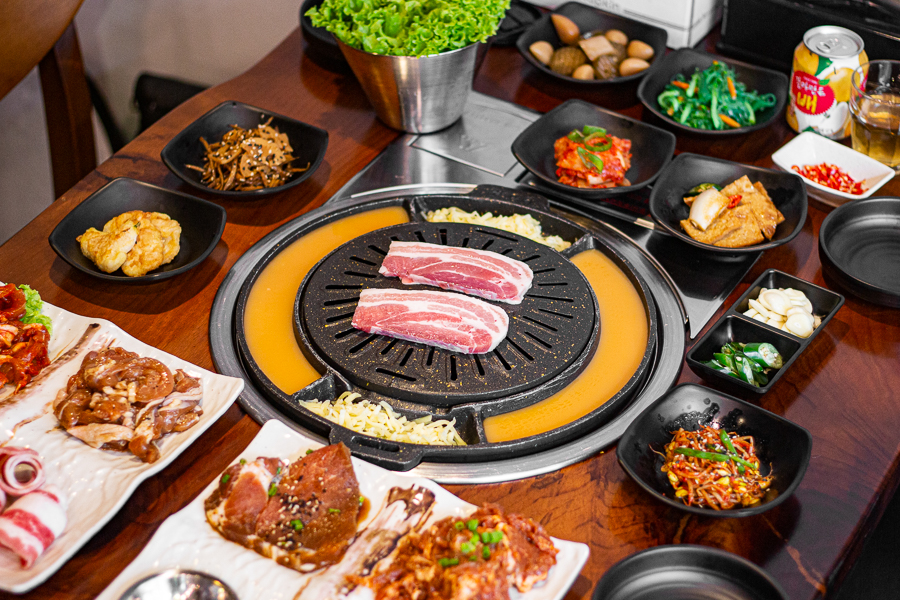 Korean BBQ Table filled with Korean side dishes and pork belly on the grill