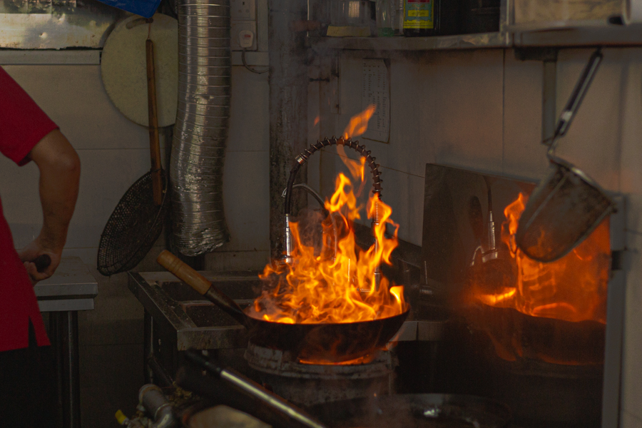 A man using a hot, fire wok to cook fried porridge at Feng Xiang BKT