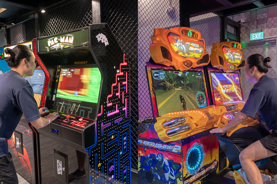 A man playing on a retro arcade and playing a seated motorbike game at a retro arcade