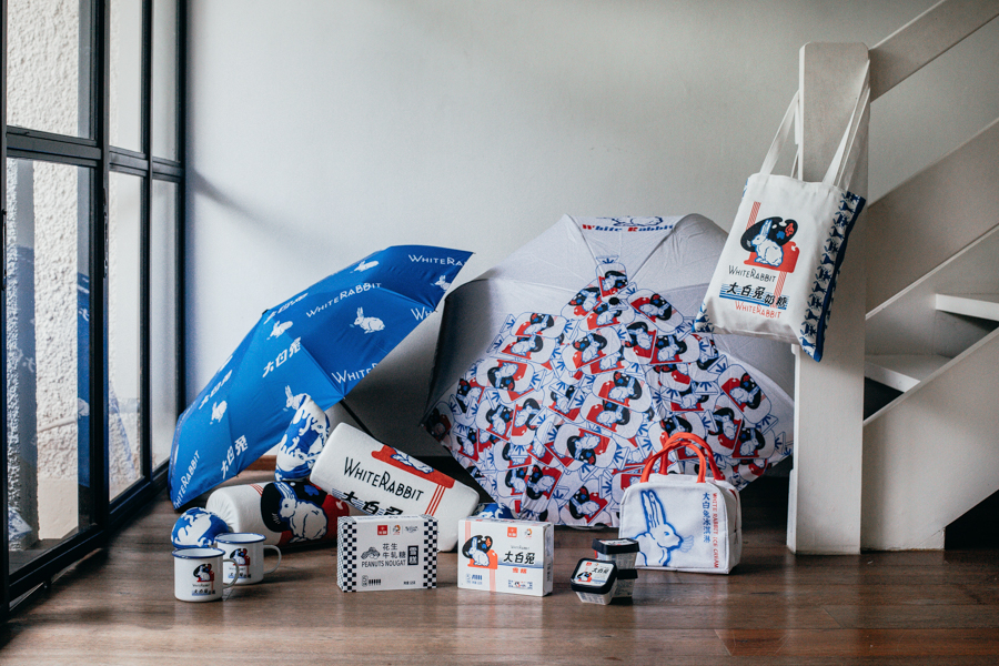 A selection of official White Rabbit Candy merchandise including umbrellas, enamel mugs, tote bags and plushies