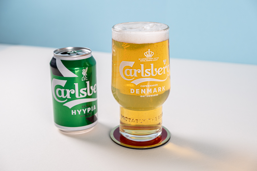 A glass of poured Carlsberg beer beside a limited edition Liverpool Football Club design jersey can