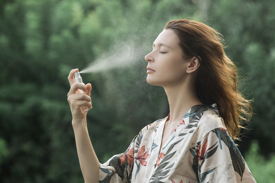 Woman spraying facial mist on her face during a hot day