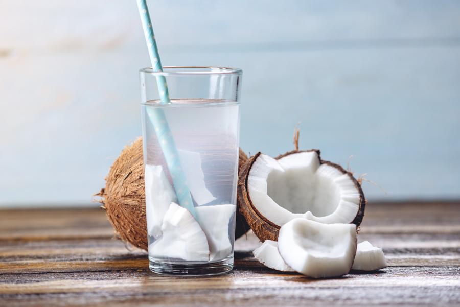 Coconut water in the composition with an open coconut with white flesh on a wooden background