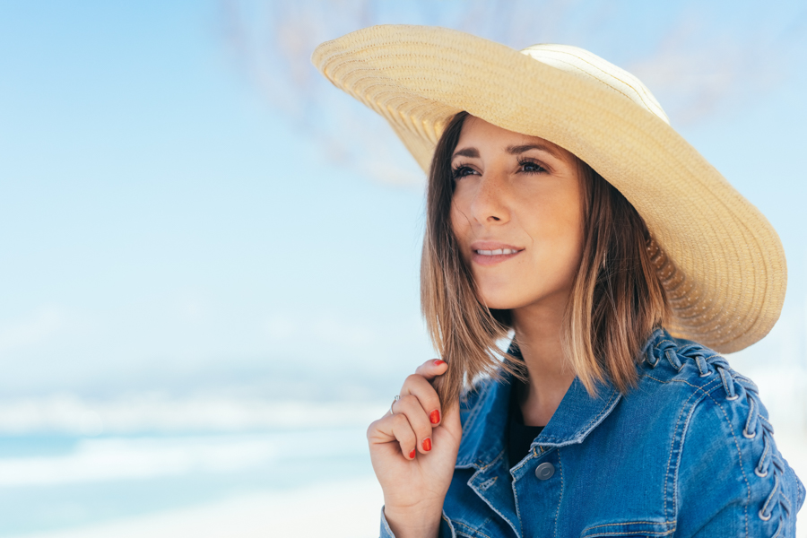 Thoughtful young woman in a wide-brimmed straw sunhat in the sun at the beach