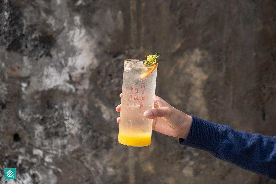 A hand with blue sweater sleeve holding a cup of Hallabong Ade